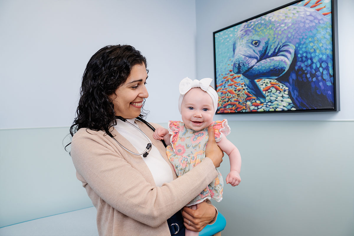 Pediatric physician holding a baby while examining the young child’s health at a pediatric primary care office in Plano, Texas