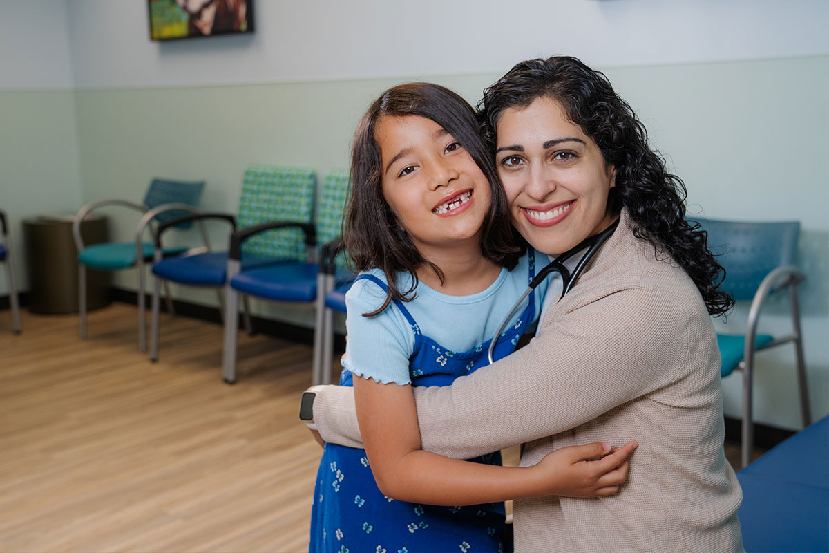 A pediatric physician hugging a patient after caring for the pediatric patient’s health